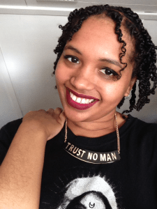 Smiling Cassandra in red lipstick with her hand on her shoulder wearing a necklace that reads Trust No Man.