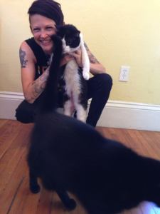 Nyxia holding up a black and white cat as another black furry creature walks out of frame.