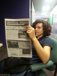 Seated zinester wearing a t-shirt reading from a paper.